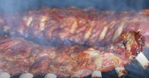 Ribs almost finished grilling, turning a deep red color with a glossy surface.