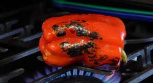 Grilling a red bell pepper, skin turning charred and blackened.