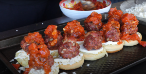 Assembling meatball sliders with bacon-wrapped meatballs topped with tomato sauce on buns, ready for grilling.