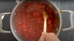 Homemade tomato sauce simmering in a stainless steel pot, stirred with a wooden spoon.