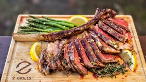 Sliced, perfectly cooked tomahawk steak served on a wooden cutting board, accompanied by fresh green asparagus and lemon slices.