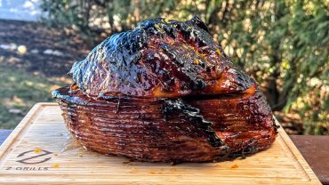 Glazed ham beautifully caramelized, presented on a wooden cutting board set against a natural outdoor backdrop.