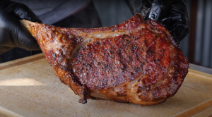 Chef in black gloves holding a perfectly seared Tomahawk steak, showcasing the rich caramelized crust and juicy interior.