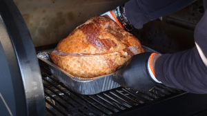 Chef placing a seasoned ham into a smoker for cooking, wearing heat-resistant gloves for safety.