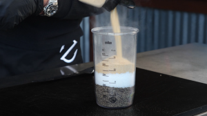 Chef mixing a custom rub for beef short ribs, pouring granulated garlic into a measuring container with layers of black pepper and salt.