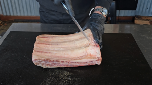 Chef trimming fat from beef short ribs on a cutting board, preparing them for smoking.