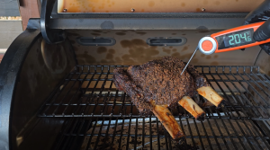 Checking the internal temperature of smoked beef short ribs on a grill, showing a reading of 204°F on a digital thermometer.