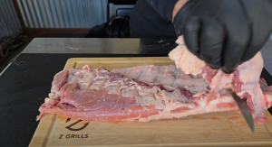 Chef skillfully trimming fat from ribs on a Z Grills cutting board, preparing the meat for smoking.