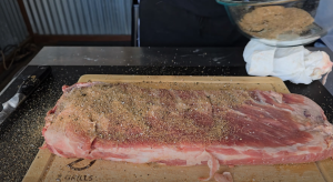 Generously applying a homemade spice rub to a prepared slab of ribs on a Z Grills cutting board.