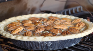 A pecan pie with whole pecans on top, freshly prepared and placed on a grill for baking.