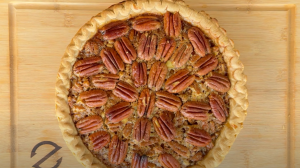 Top view of a perfectly baked pecan pie with a golden crust and neatly arranged pecan halves on a Z Grills wooden cutting board.