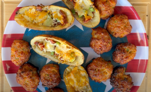 An array of grilled Super Bowl appetizers on a serving platter, featuring candied bacon, smoked sausage balls, and stuffed loaded potato skins.