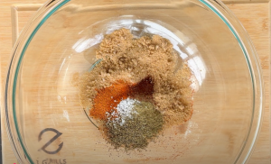 A blend of spices in a mixing bowl, ready for seasoning beer can chicken, showcasing brown sugar, chili powder, paprika, dry mustard, garlic and onion powders.