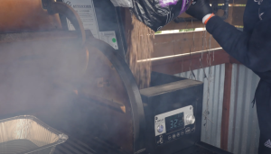 Pouring wood pellets into a Z Grills smoker, smoke billowing as the grill heats up, preparing for a barbecue session.