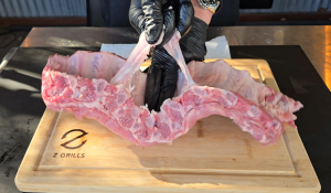 Preparing baby back ribs by removing the membrane on a wooden cutting board, highlighting the initial steps for perfect rib preparation.