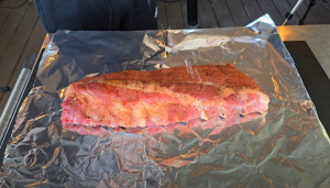 Fresh baby back ribs seasoned with a custom spice blend on foil, ready for smoking.