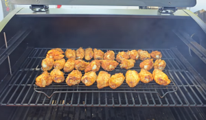 Seasoned chicken wings cooking on the middle rack of a Z Grills pellet grill with light smoke rising.