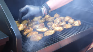 Grillmaster flipping smoked chicken wings over direct heat on a Z Grills pellet grill as smoke rises