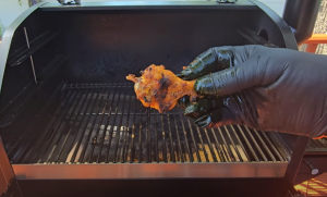 A gloved hand holding a fully cooked, charred buffalo wing fresh off the grill.