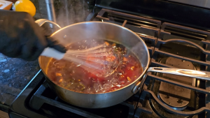 Honey orange glaze being whisked in a saucepan over a gas stove, releasing steam.