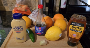 Ingredients for honey orange glaze including Dijon mustard, soy sauce, jalapeño, garlic, lemon, oranges, and honey on a cutting board.