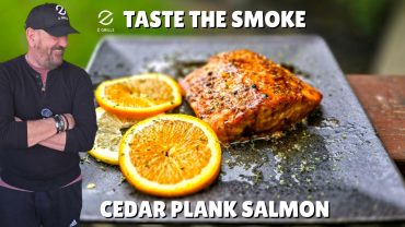 Grilled cedar plank salmon served with orange slices on a black plate, with text “Taste the Smoke – Cedar Plank Salmon.”