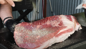 Raw brisket being seasoned with kosher salt, black pepper, and granulated garlic before going on a Z Grills pellet smoker.