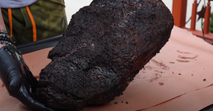 Fully smoked brisket with a dark, crusty bark being transferred to butcher paper after 14 hours on a pellet smoker.
