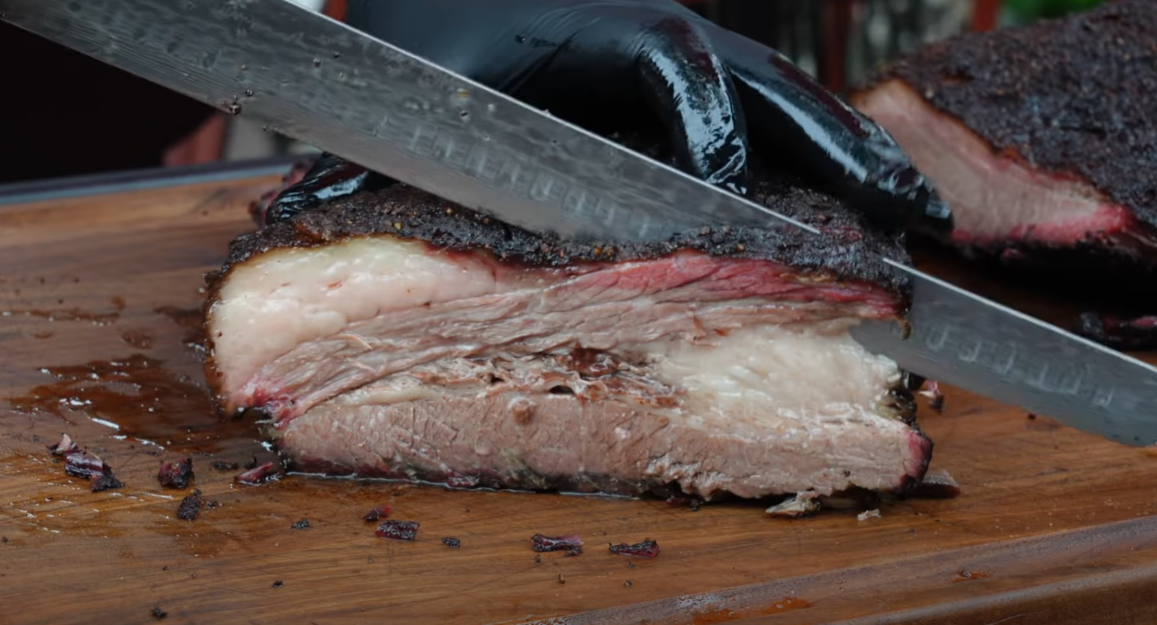 Juicy sliced brisket showing smoke ring, bark, and rendered fat layers, being cut with a slicing knife on a wooden board.