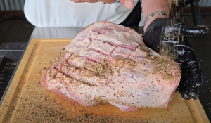 Cross-scored pork shoulder seasoned with salt, pepper, and garlic on a wooden cutting board.