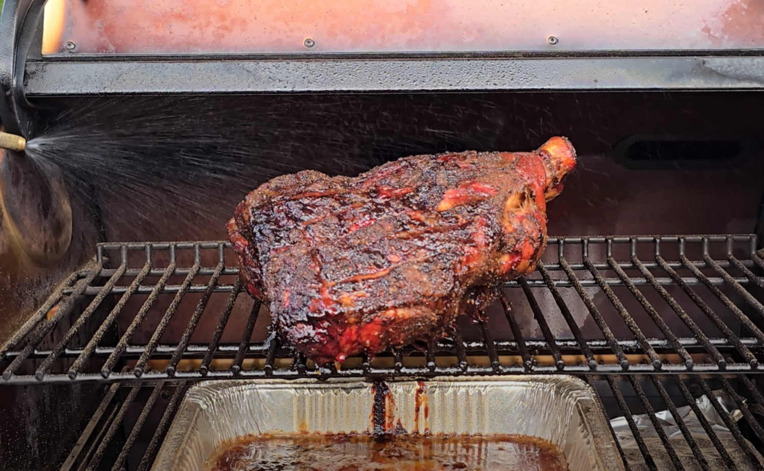 Smoked pork shoulder resting on a pellet grill with a drip pan catching juices below.