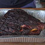 Smoked pork shoulder resting in a foil pan after cooking, ready to be pulled.