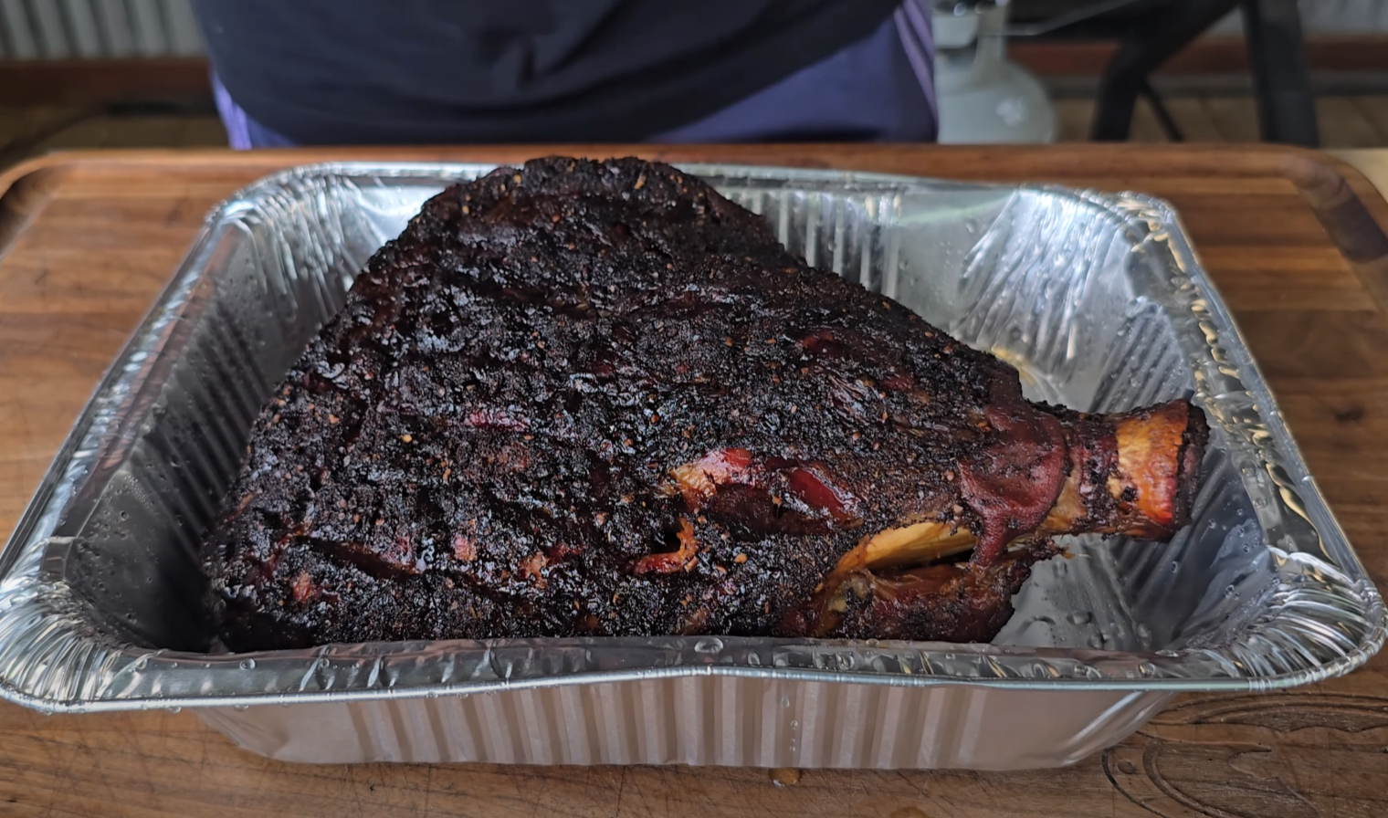 Smoked pork shoulder resting in a foil pan after cooking, ready to be pulled.