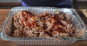 Shredded smoked pork shoulder in a foil pan topped with barbecue sauce.