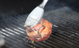 Bacon-wrapped filet mignon being basted with garlic butter on a pellet grill