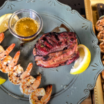 Grilled shrimp skewers and bacon-wrapped filet mignon served with garlic butter and lemon wedges