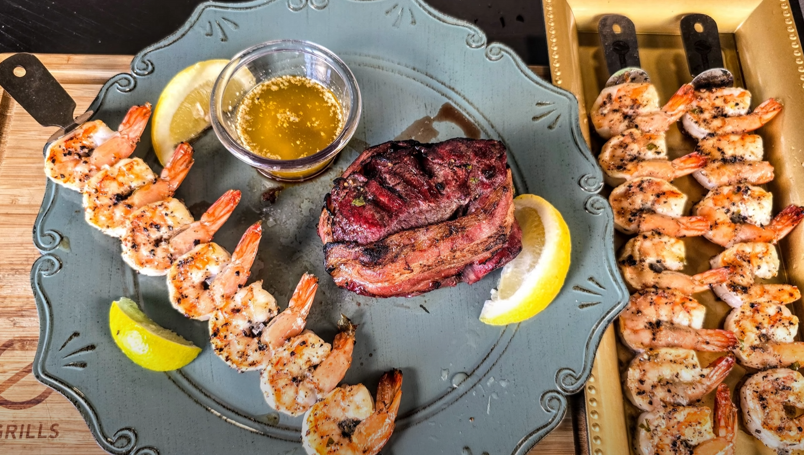 Grilled shrimp skewers and bacon-wrapped filet mignon served with garlic butter and lemon wedges