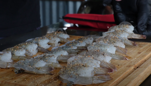 Raw jumbo shrimp seasoned with dry rub on a wooden cutting board