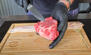 Chef trimming filet mignon before wrapping it in bacon on a wooden Z Grills cutting board