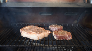 Ribeye and filet mignon steaks smoking on a Z Grills pellet grill grate.
