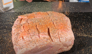 Pork butt with a scored fat cap being seasoned with BBQ rub.