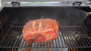 Seasoned pork butt smoking on a pellet grill.