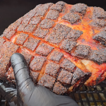 Gloved hand holding smoked pork butt with a dark, crosshatched bark.