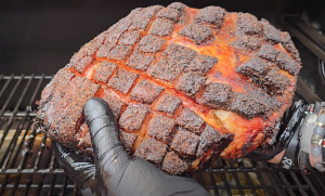 Gloved hand holding smoked pork butt with a dark, crosshatched bark.