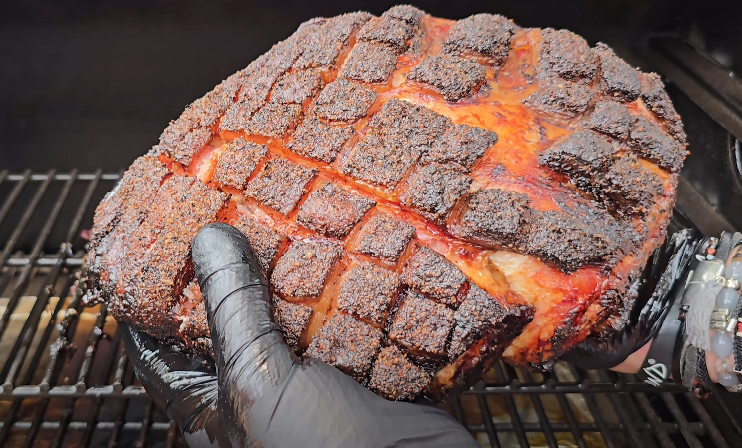 Gloved hand holding smoked pork butt with a dark, crosshatched bark.
